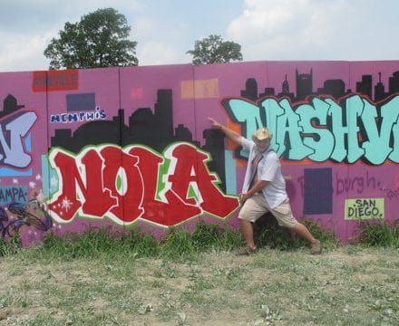 A man in a goofy hat hugs some NOLA graffiti at Bonnaroo.